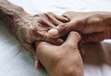 Two hands of younger person holds one hand of on eldery, on white sheets