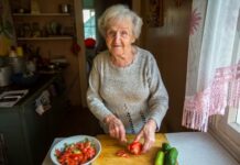 Oudere dame snijdt tomaten en komkommers in een keuken: eten en drinken bij dementie.