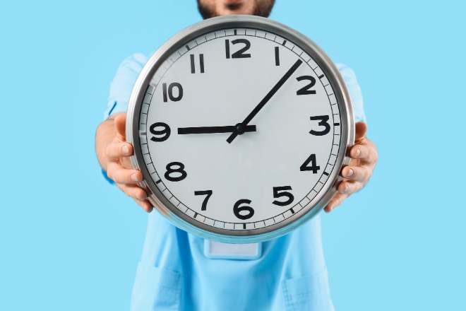 © Pixel-Shot / Stock.adobe.com Grote klok tegen blauwe achtergrond, vastgehouden met handen door een man, wiens gezicht je niet ziet. Bij artikel over overuren compenseren in BalansBudget.